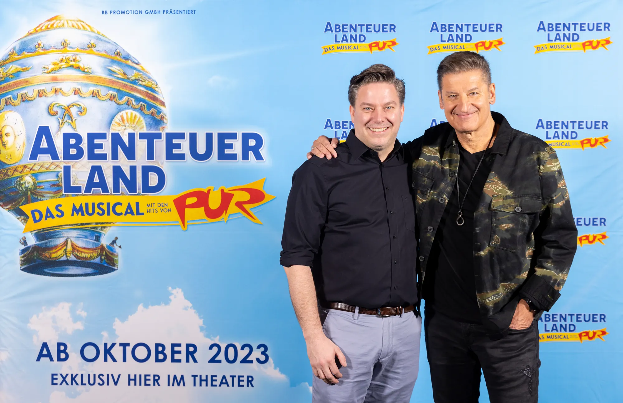Musical Düsseldorf - Abenteuerland Pressekonferenz mit Martin Flohr und Hartmut Engler Arm in Arm und lächelnd vor dem Abenteuerland Logo