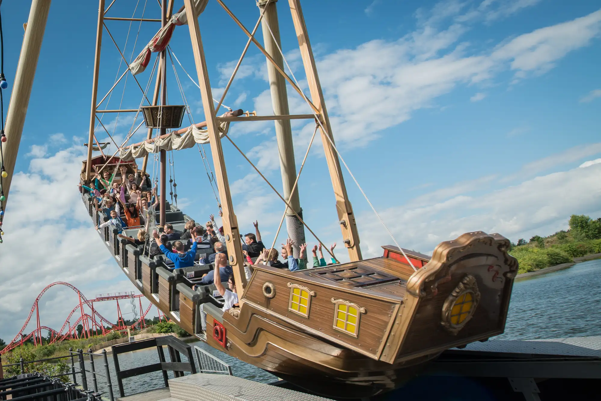 Belantis Park - Santa Maria Schiffschaukel in Fahrt mit Menschen die die Hände in die Höhe reißen vor dem See im Freizeitpark