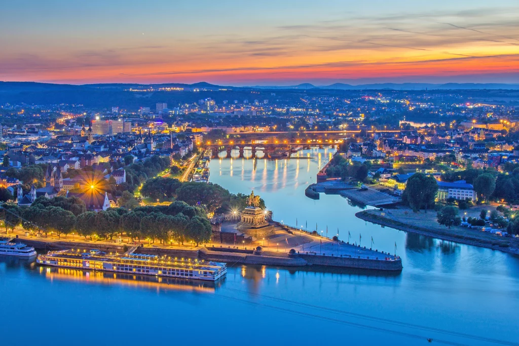 Illuminierter Panoramablick auf das Deutsches Eck in Koblenz in der Abenddämmerung